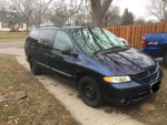2000 Dodge Caravan parked with a roof rack, showing some rust and scratches, good for commuting.