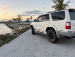 2002 Toyota 4Runner SR5 RWD parked by a waterfront during sunset, showcasing its sleek design and black rims.