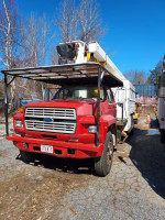 1989 Ford F700 Versalift truck with a lift, well-maintained for local seasonal use, parked in a wooded area.