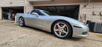 2006 Chevrolet Corvette C6 Z51 in silver with custom exhaust and LED lights, parked outside a garage.