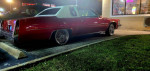 1997 Cadillac DeVille in candy apple red parked under lights with chrome wire wheels