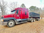 2002 Freightliner Century truck with a 20 ft dump trailer parked on a dirt road, surrounded by trees.