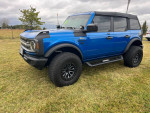 Blue 2022 Ford Bronco Big Bend 4WD with 35-inch tires parked on grass, showcasing custom rims and off-road features.