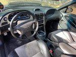 Interior view of a 1994 Ford Mustang GT with black leather seats and dashboard, showcasing gauges and controls.