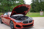 2020 BMW M850i xDrive convertible in Sunset Orange with hood open showcasing the engine.