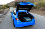 Open trunk of a blue 2024 Honda Civic Sport on a rural road, showcasing spacious storage.