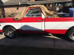 1969 GMC 1500 pickup truck in red and white, with storage tarp, parked in a garage.