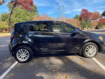 2014 Chevrolet Sonic LT hatchback in black with aluminum wheels parked outdoors with autumn foliage.