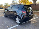 2014 Chevrolet Sonic LT hatchback in black with aluminum wheels, parked in a leafy area, showing rear view.