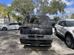 Front view of a 1995 Nissan Homy van parked among palm trees, showcasing its unique design and condition.