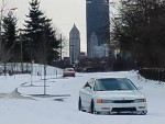 1994 Honda Accord coupe parked on a snow-covered street with city skyline in the background.