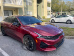 2023 Kia K5 GT in passion sport red, parked outside residential building.