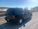 Black 2003 GMC Yukon Denali parked by the river, showcasing its sleek design and AWD features.