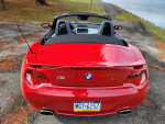Rear view of a red BMW Z4 M Roadster parked by a serene lake, showcasing low mileage and stunning condition.