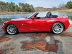 Red BMW Z4 M Roadster parked by a lake, showcasing its sleek design and low mileage.