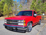 1989 Chevrolet Silverado C1500 Pickup in red parked outdoors with chrome wheels and trees in background.