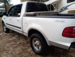 Side view of a white Ford F-150 truck, showcasing its spacious cab and pickup bed, parked outdoors.