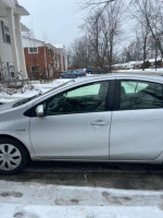 Side view of a silver 2014 Toyota Prius C parked on a snowy street, showcasing its well-maintained exterior.