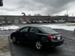 2013 Toyota Corolla LE FWD in black, parked outdoors with snow in the background, showcasing its great condition.