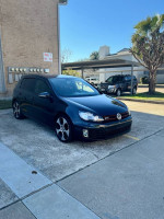 Black Volkswagen Jetta GTI parked, showcasing its clean design and alloy wheels, with blue sky background.