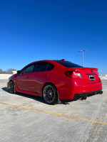 2016 red Subaru WRX Limited AWD parked, showcasing modified wheels and sleek design against a blue sky.