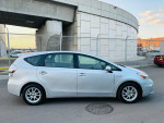 2012 Toyota Prius V Three parked near a modern building, showcasing its sleek design and alloy wheels.