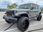 Customized 2019 Jeep Wrangler Unlimited Sahara with lifted suspension and large black rims in a parking lot.