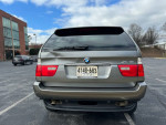 Rear view of a 2006 BMW X5 3.0i AWD with a dent on trunk in a parking lot.