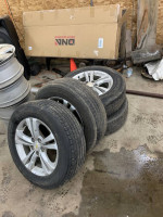 Four used tires stacked with Chevrolet rims in a garage setting, ready for sale.