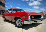 1973 Chevrolet Nova Custom Sedan in red, showcasing a classic design and polished chrome wheels against a clear sky.