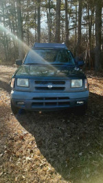 2000 Nissan Xterra SE RWD in a forest setting with a damaged passenger front panel.