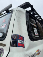 Close-up of a modified Toyota Landcruiser with stickers, showcasing its rugged features and body damage.