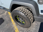 Close-up of a lifted 2014 Jeep Wrangler tire with black and green wheels on asphalt.