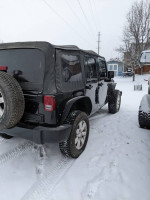 Black 2014 Jeep Wrangler Sahara 4WD parked in snowy conditions, showing good tire tread and exterior condition.