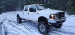 2001 Ford F350 Crew Cab with 8" lift and new turbo, parked in snow-covered forest trail.