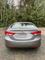 Rear view of a 2013 Hyundai Elantra GLS in excellent condition, surrounded by trees