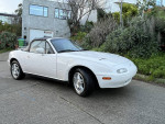 1994 Mazda Miata MX-5 with 177,000 miles, parked in a driveway surrounded by greenery.