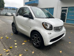 2016 Smart Fortwo Pure in white, compact car with aluminum wheels, parked outdoors among fallen leaves.