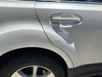 Close-up of a white 2013 Subaru Outback showing door damage and wear, highlighting salvage title condition.