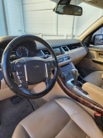 Interior view of a 2013 Land Rover Range Rover with beige leather seats and wood trim, showcasing the dashboard and steering wheel.