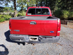 Rear view of a 2002 Ford F250 Super Duty truck in red, showcasing the bed and logo.