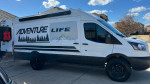 2017 custom Ford Transit 250 motovan with Adventure Life graphics and off-road tires parked outdoors