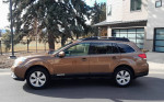 2012 Subaru Outback 2.5i AWD in brown color, parked in front of a modern building.