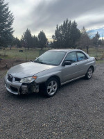 Silver Subaru Impreza with body damage parked on gravel, well maintained with clean interior, ideal for parts or repair.