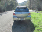 Rear view of a 2006 Subaru WRX wagon parked on a gravel road surrounded by greenery.