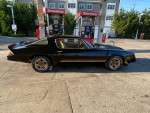 1980 Chevy Camaro Z28 in black, parked at a gas station, showcasing its classic design and shiny wheels.