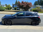 Profile view of a 2010 Mazdaspeed3 with custom features and adjustable coilovers, parked on a sunny street.