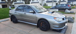 2007 Subaru Impreza WRX STI in silver parked on a driveway, showcasing its sporty design and black wheels.