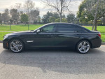 Side view of a black 2015 BMW 750Li M Sport parked in a green area, showcasing its sleek design and alloy wheels.