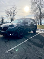 2019 Honda Passport Sport FWD parked under the sun with trees in the background, showcasing its sleek black design.